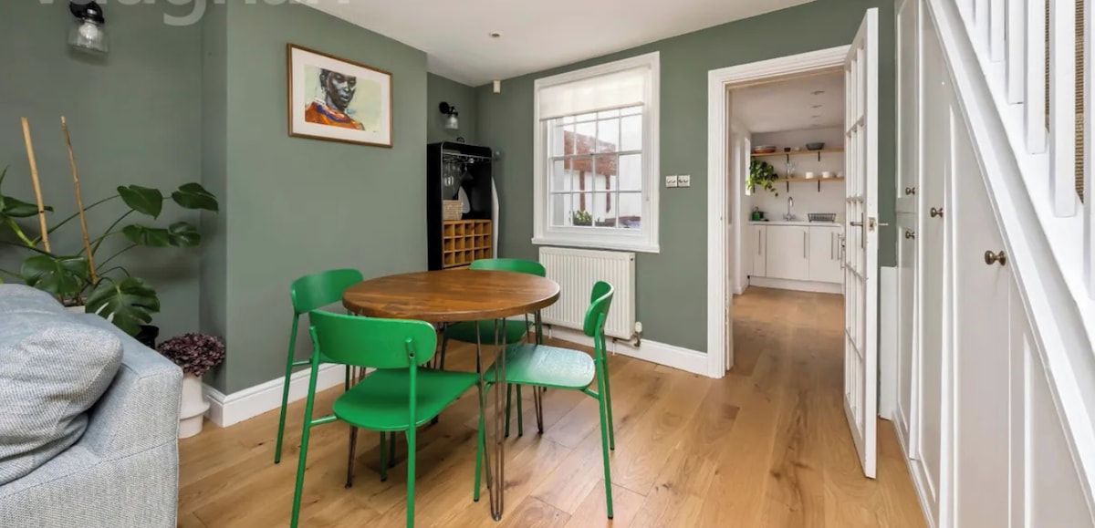 A light, well-defined dining area with a wooden table and bright green chairs that add colour and character. Thoughtfully placed artwork and good natural light create a relaxed setting, clearly separated from the kitchen for comfortable meals.