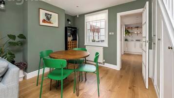 A light, well-defined dining area with a wooden table and bright green chairs that add colour and character. Thoughtfully placed artwork and good natural light create a relaxed setting, clearly separated from the kitchen for comfortable meals.