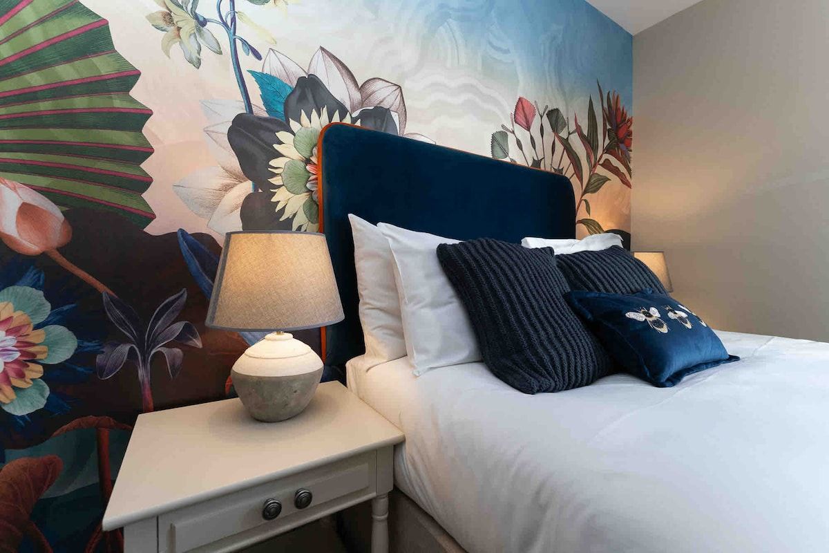 Una habitación de hotel con una cama, una mesita de noche con una lámpara y un mural floral en la pared.