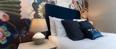 Una habitación de hotel con una cama, una mesita de noche con una lámpara y un mural floral en la pared.