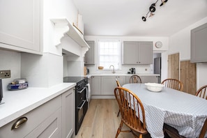 A compact kitchen with white cabinetry, a built-in oven, a dining table with chairs, and a window above the sink. - Seaside Historic Townhouse, 1 Min to Beach, (Worthing)