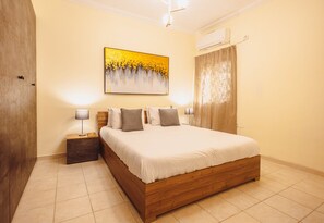 A hotel room with a large bed, two bedside tables, a wall-mounted air conditioner, and a painting above the bed. - Spacious 2BR Sliema Apartment (Sliema)