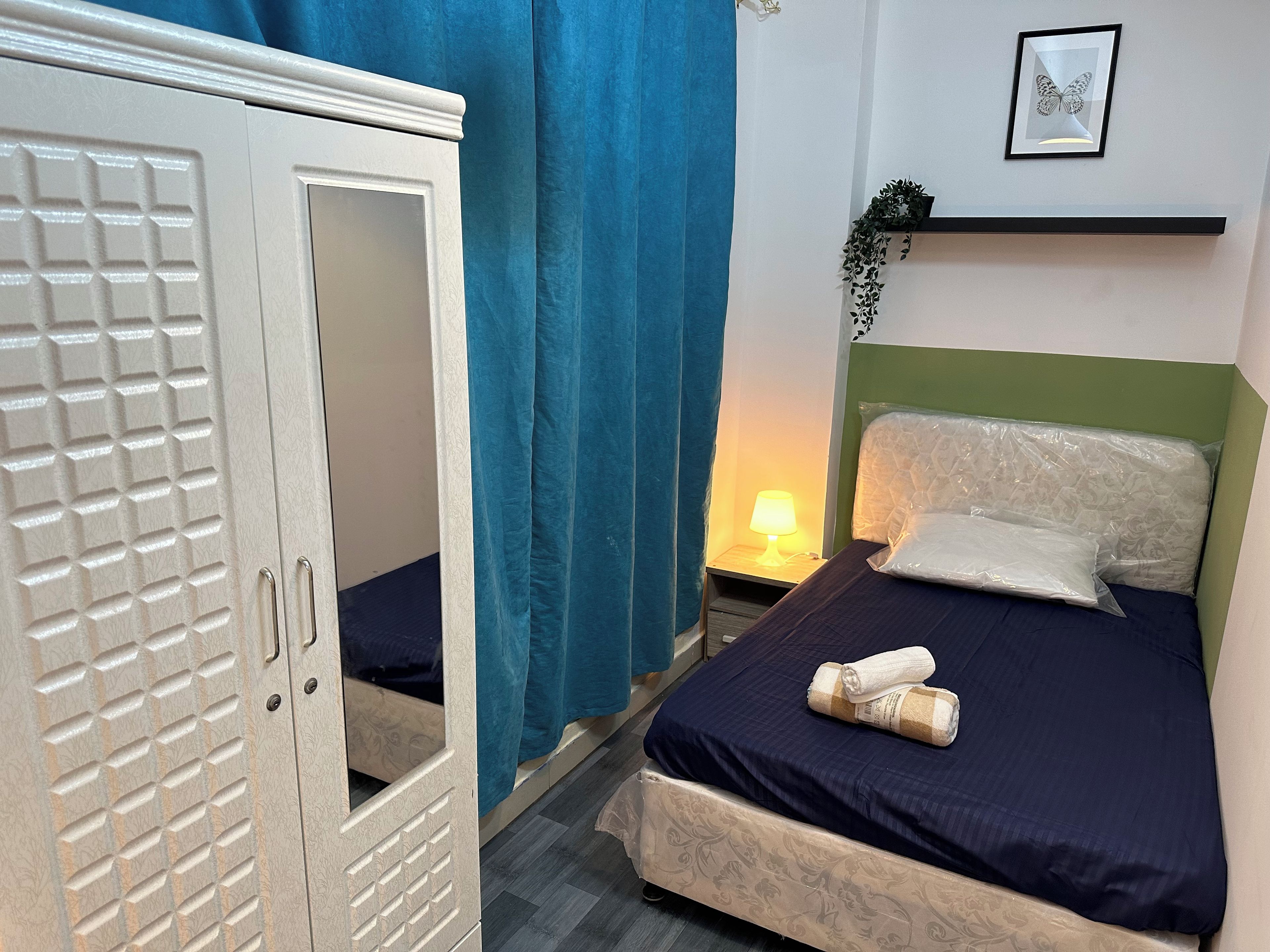 Een slaapkamer met een bed, nachtkastje, lamp, garderobe en een lijst met een vlinder afbeelding.