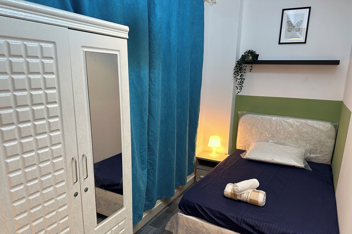 A bedroom with a bed, a nightstand, a lamp, a wardrobe, and a framed butterfly picture on the wall.