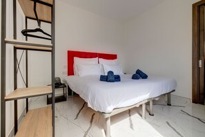 A neatly made bed with white bedding and blue towels, a red headboard, and a wooden floor. - Trendy 3BR Home by the Waterfront (Gzira)