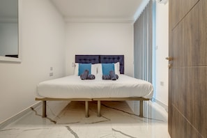 A bedroom with a bed, a wooden wardrobe, and a bathroom door. - Stylish 3BR Maisonette by the Promenade (Gzira)