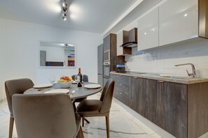 A modern kitchen with a dining area, featuring a round table, chairs, and a view of the city through a large window. - Stylish 3BR Maisonette by the Promenade (Gzira)