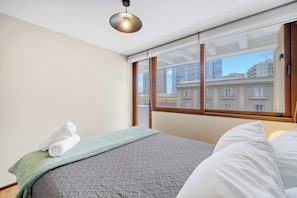 A bedroom with a bed, a window, and a view of buildings. - Acogedor departamento bohemio en Providencia (Providencia)