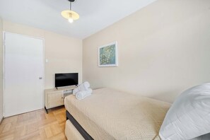 Une chambre à coucher comprenant un lit, un téléviseur, une œuvre d’art accrochée au mur et une porte.