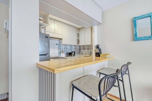 A modern kitchen with a wooden countertop, two bar stools, and a patterned backsplash. - Acogedor departamento bohemio en Providencia (Providencia)