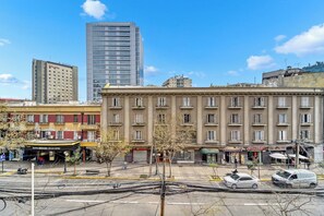 A multi-story building with a flat facade, a parking lot in front, and a clear blue sky. - Acogedor departamento bohemio en Providencia (Providencia)