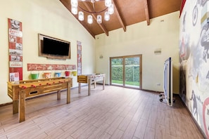 A spacious room with wooden flooring, a foosball table, a television mounted on the wall, and a large window providing a view of greenery outside. - Casa Alicura con Patio a pasos del Centro de Pucón (Pucon)