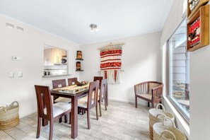 A dining area with a wooden table and chairs, a woven wall hanging, and a window with blinds. - Casa Alicura con Patio a pasos del Centro de Pucón (Pucon)