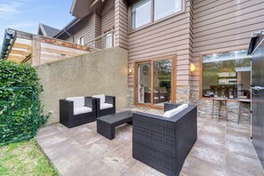 A patio with outdoor furniture, a stone wall, and a view of the house interior through a glass door. - Casa Alicura con Patio a pasos del Centro de Pucón (Pucon)