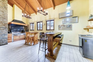 Eine Küche mit Steinwand, Holzboden und einem eingebauten Backofen. Es sind Holzstühle und ein Tisch vorhanden, und ein Kühlschrank ist sichtbar.