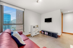 Een moderne woonkamer met een rode bank, een flatscreen televisie aan de muur en uitzicht op een stadsgezicht door grote ramen.