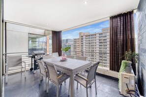 Un balcón con mesa y sillas, una parrilla y vistas a la ciudad.