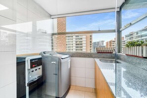 Een moderne keuken met een ingebouwde wasmachine en droger, een granieten aanrechtblad en uitzicht op de stad.