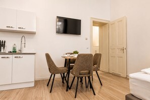 Een moderne keuken met witte kasten, een flatscreen televisie en een eethoek met vier stoelen.