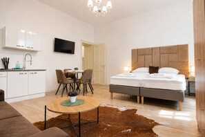 A modern bedroom with a large bed, a wooden headboard, a dining area with chairs, a kitchen with white cabinets, and a television mounted on the wall. - Vienna City Escape Studio near Belvedere (Vienna)