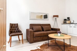 Een moderne woonkamer met een bruine leren fauteuil, een bruine bank, een ronde houten salontafel en een koperen vloerkleed.