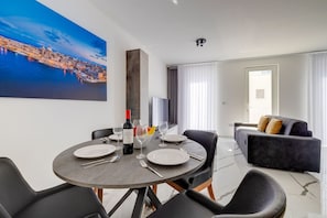 A dining area with a round table, chairs, a wine bottle, and a painting of a cityscape. - Spacious 3BR Residence by the Promenade (Gzira)