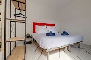 A hotel room with a bed, a nightstand, a red headboard, and a wooden shelf unit. - Spacious 3BR Residence by the Promenade (Gzira)