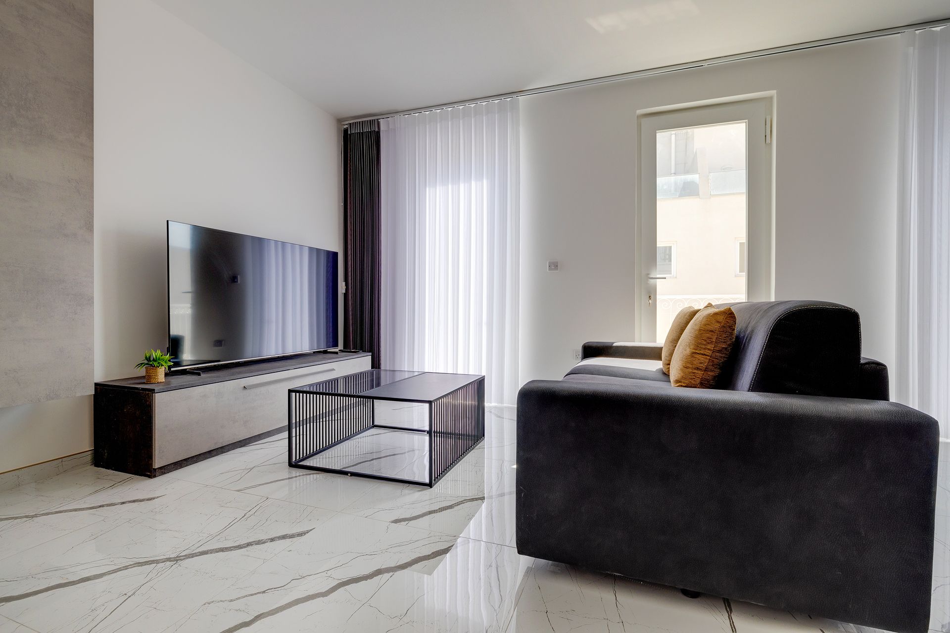 Een moderne woonkamer met een flatscreen televisie, een glazen salontafel en een donkere bank met kussens.