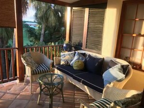 Een balkon met rieten meubels, een glazen tafel en uitzicht op palmbomen.