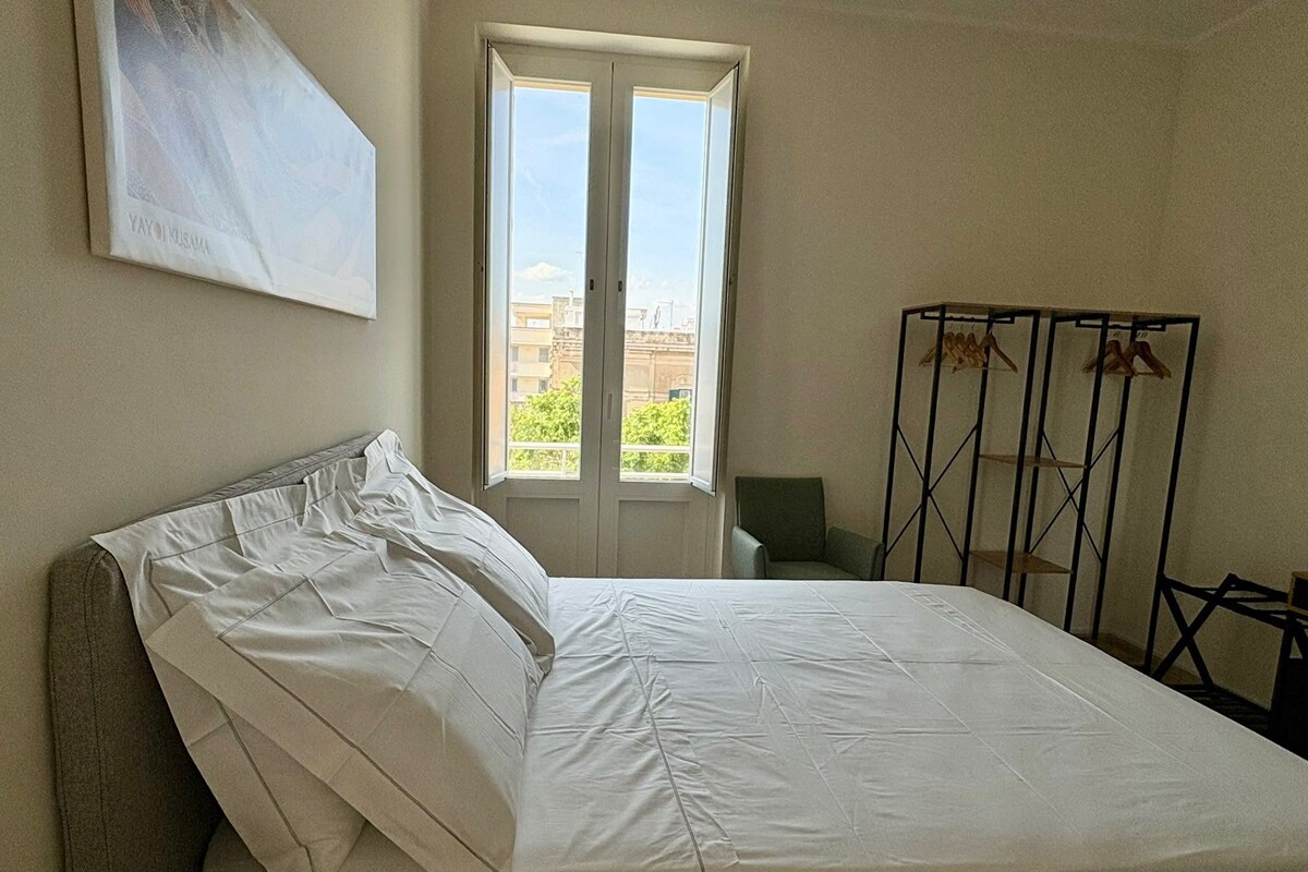 Een slaapkamer met een bed, een raam en een droogrek.