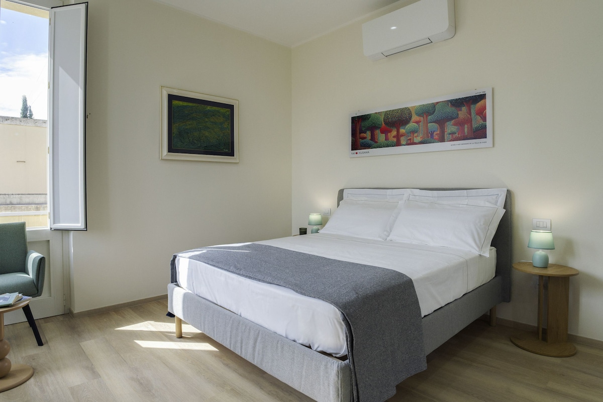 A hotel room with a bed, a chair, a window, and two wall-mounted lamps.