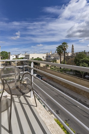 A balcony with a metal chair, overlooking a street with cars and buildings, including a tower. - Dimora Donnalia (Lecce)