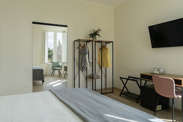 A hotel room with a bed, a desk, a chair, a TV, and a clothing rack. - Dimora Donnalia (Lecce)