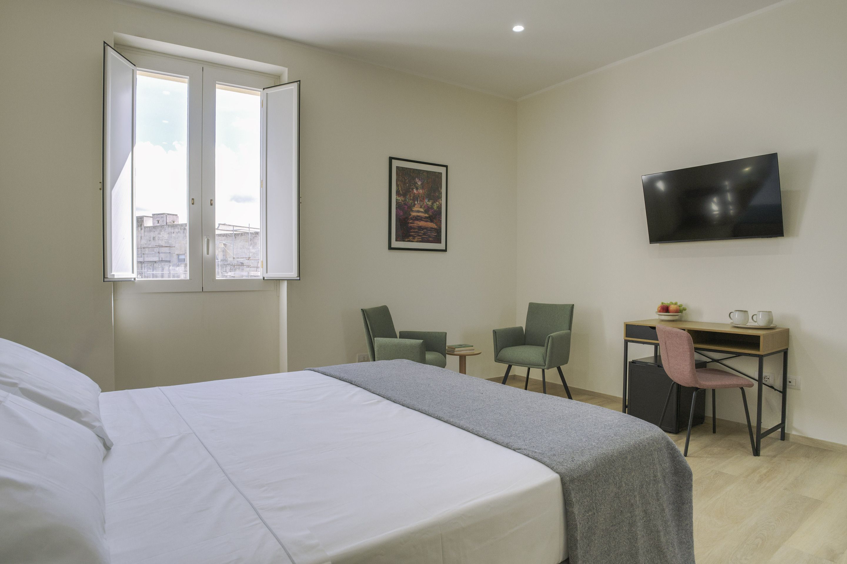 A hotel room with a bed, a desk with a chair, a television, and a window.