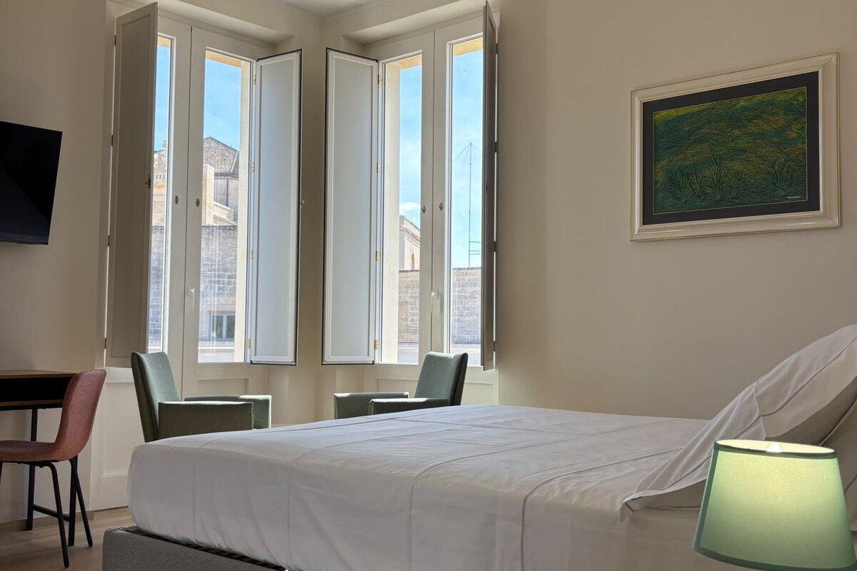 Een hotelkamer met een bed, een bureau, een stoel, een ronde tafel met een lamp en een schilderij aan de muur.