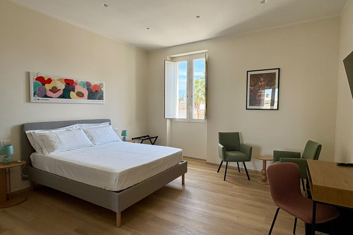 Een slaapkamer met een bed, een bureau, stoelen, een raam en kunst aan de muren.