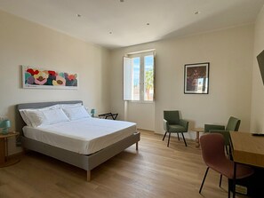 Een slaapkamer met een bed, een bureau, stoelen, een raam en kunst aan de muren.