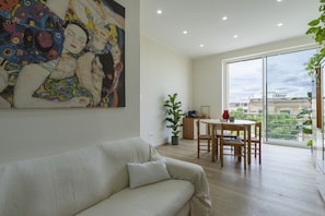 A living room with a sofa, a dining table with chairs, a large painting on the wall, and a view through a glass door. - Dimora Donnalia (Lecce)
