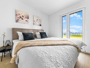 A bedroom with a large bed, a nightstand, a lamp, and two wall-mounted artworks. - Apartment in Olpenitz With Swimming Pool (Kappeln)