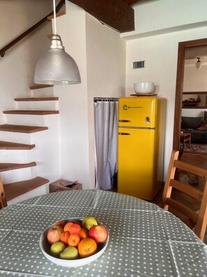 A room with a dining table, a yellow refrigerator, a staircase, and a ceiling light. - Natural Stone House with a Pool and Ocean View in the Maremma (Prata)