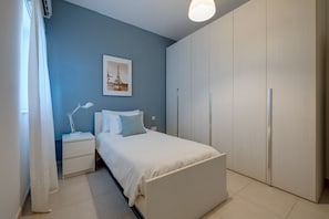 A bedroom with a bed, a nightstand, a lamp, a wardrobe, and a picture of the Eiffel Tower on the wall. - Seaside Bliss - 3BR Holiday Apartment, Sliema (Sliema)