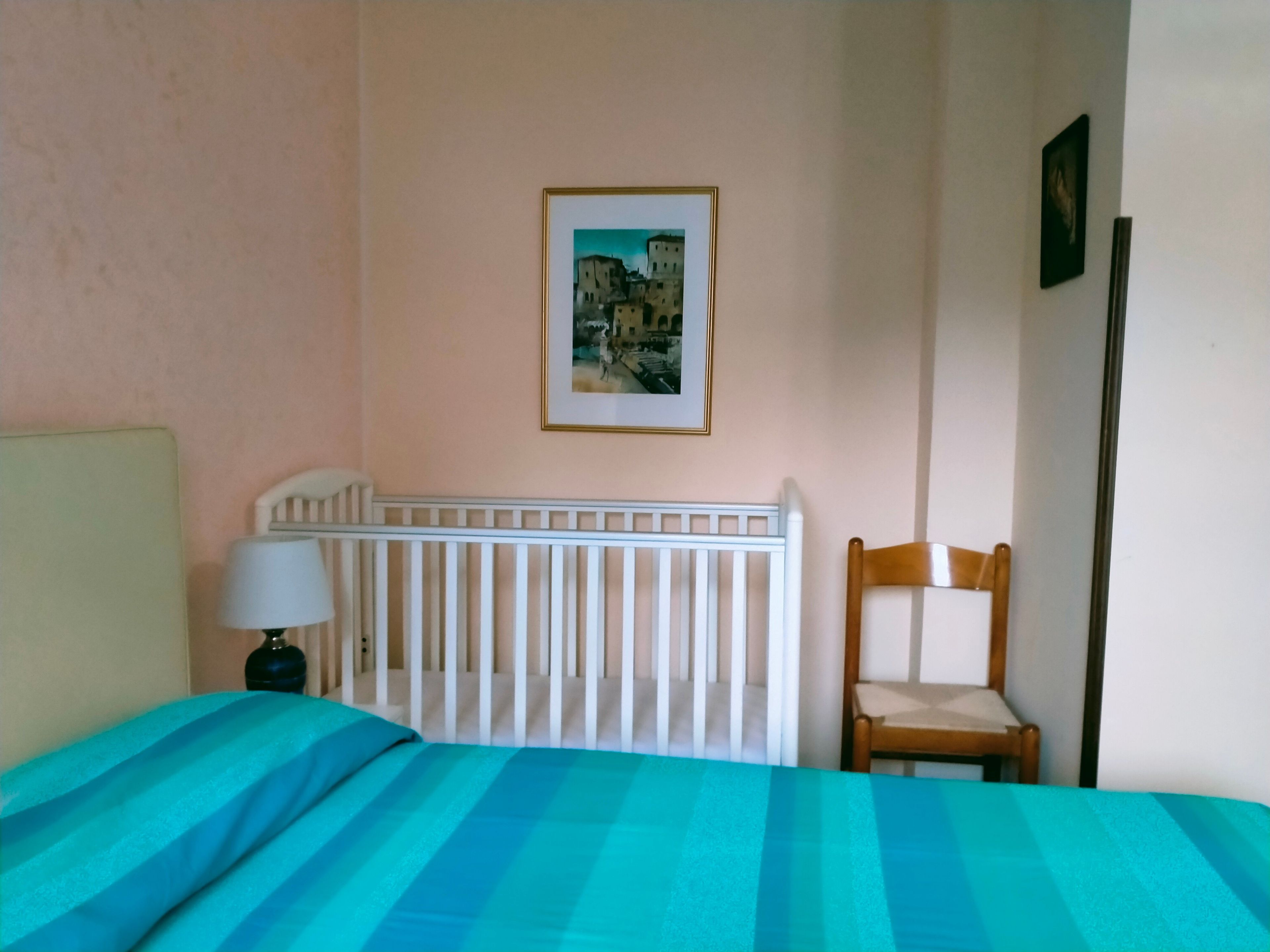 Una habitación con cama, una silla, una cuna y un cuadro colgado en la pared.