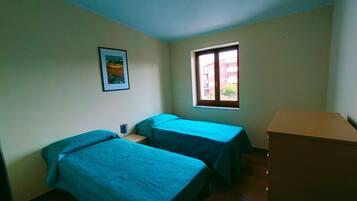 Ein Zimmer mit zwei Betten, einem Fenster, einem Bild an der Wand und einem Holzschrank.