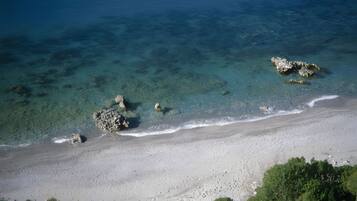 Ein Strand mit klarem Wasser, Felsen und einem Sandufer.