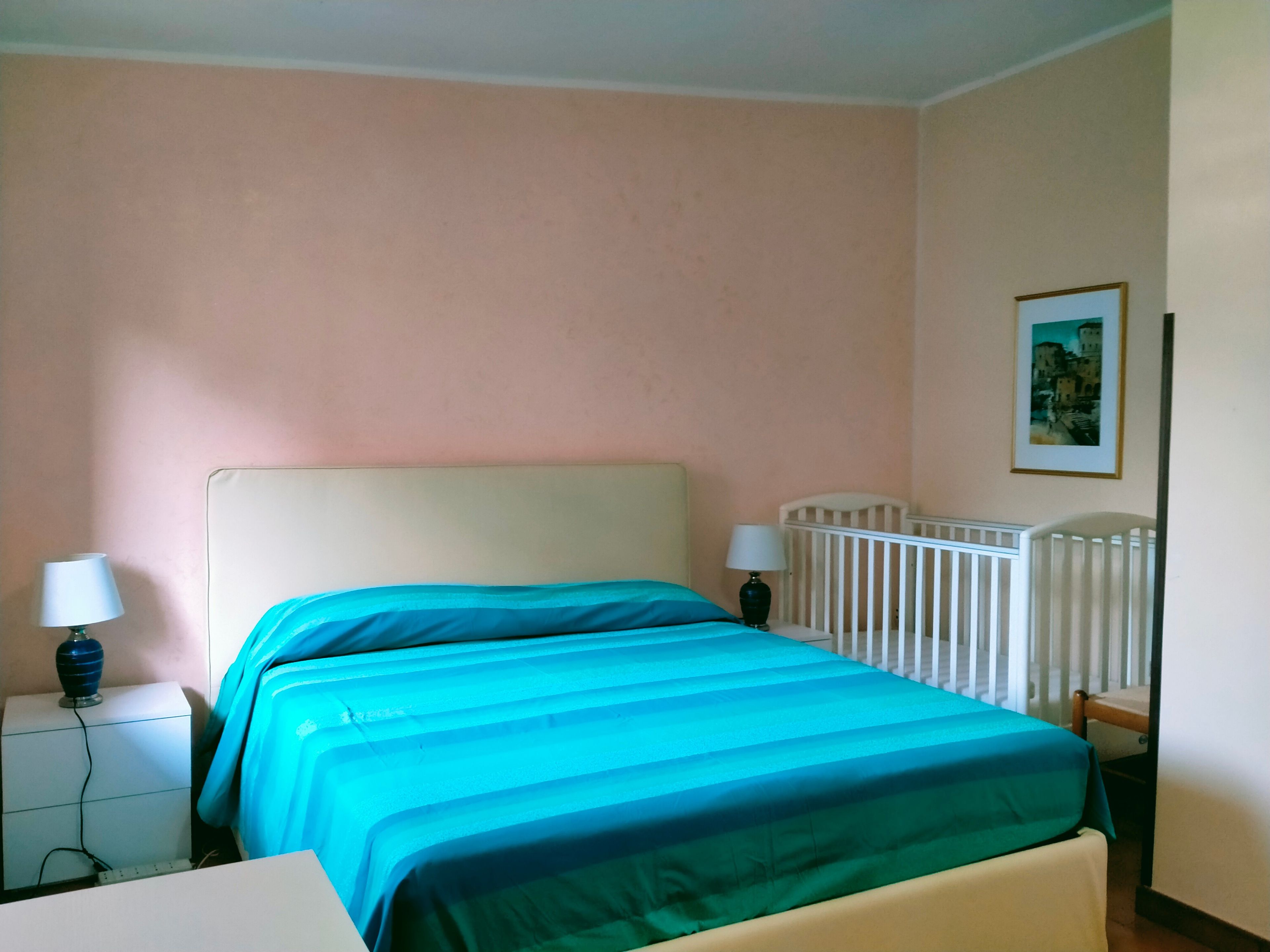 Ein Schlafzimmer mit Bett, Nachttischen, einem Babybett und einem Wandbild.