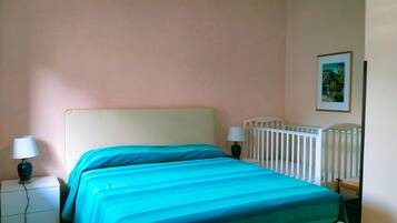 Ein Schlafzimmer mit Bett, Nachttischen, einem Babybett und einem Wandbild.
