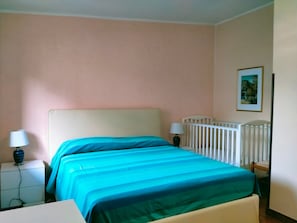 Ein Schlafzimmer mit Bett, Nachttischen, einem Babybett und einem Wandbild.