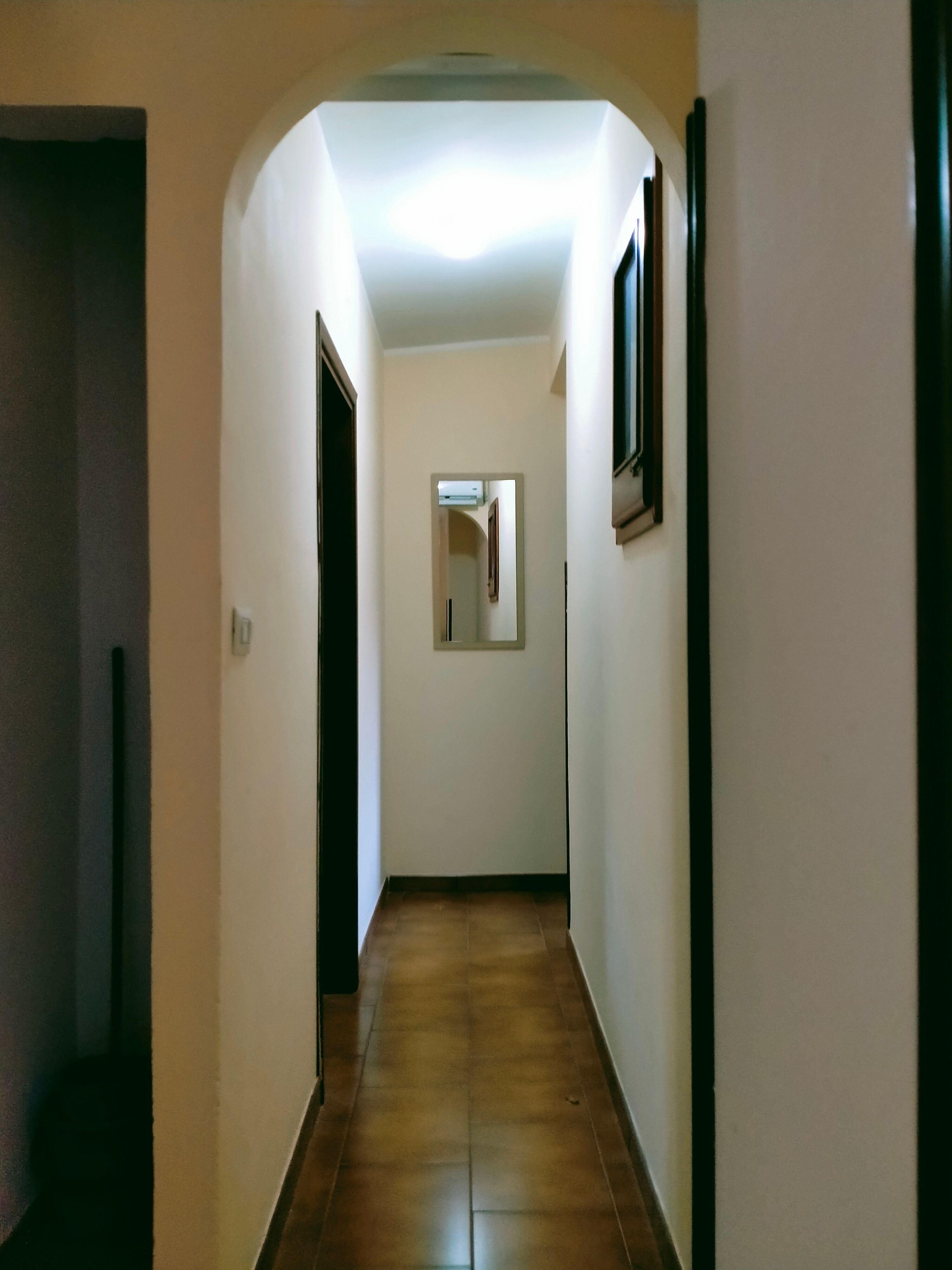 Un corridoio stretto con pavimento piastrellato, un quadro appeso al muro e una porta a sinistra.