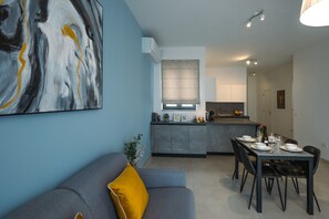 A modern kitchen with a dining area, a grey sofa with a yellow pillow, and a large abstract painting on the wall. - Bright and Modern 2BR Penthouse, St Julian's (St. Julian's)