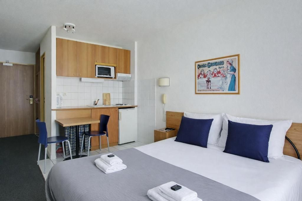 Une chambre d’hôtel avec un lit, un bureau, une chaise, un micro-ondes et une affiche au mur.